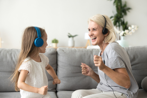 Excited woman nanny listening to music and dancing with young girl
